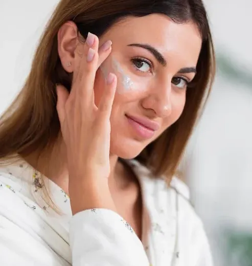 Mulher aplicando creme facial em frente ao espelho